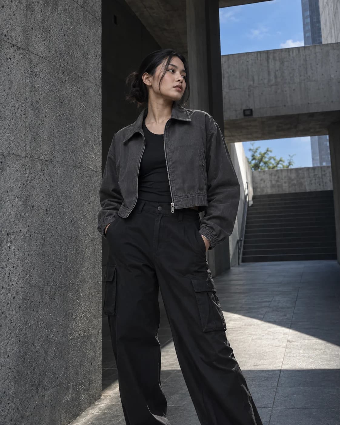 Woman wearing a graphite crop jacket in a concrete passage